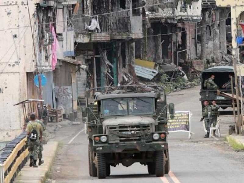 Soldati filippini presidiano un ponte, sullo sfondo i palazzi distrutti dai bombardamenti a Marawi (foto LaPresse)