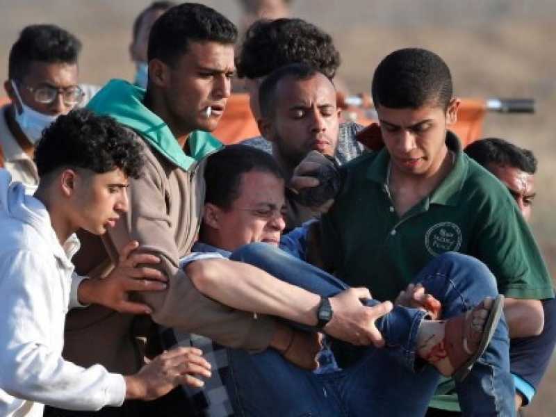 Un gruppo di palestinesi trasporta un ferito durante gli scontri a Gaza (foto LaPresse)