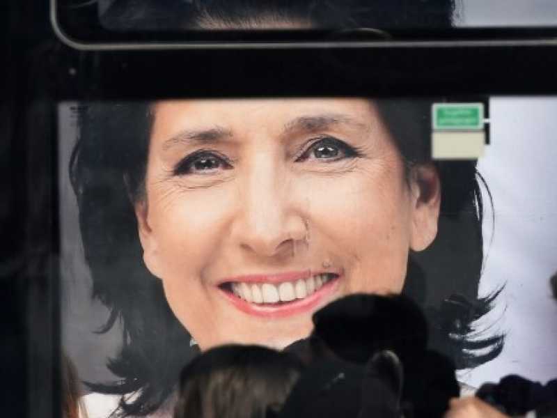 Pendolari su un autobus davanti a un manifesto elettorale del candidato presidenziale Salome Zurabishvili a Tbilisi (foto LaPresse)