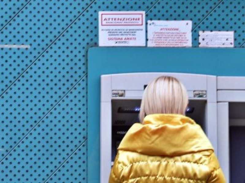 Una donna preleva contanti in uno sportello bancomat di una banca Carige (foto LaPresse)