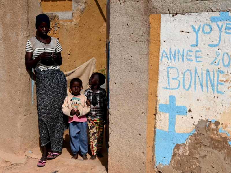 Una donna e dei bambini vicino alla scritta murale &ldquo;Buon Natale 2018/2019, buone feste&rdquo; nel villaggio di Yagma, a nord di Ouagadougou, il 17 settembre 2019 (LaPresse)