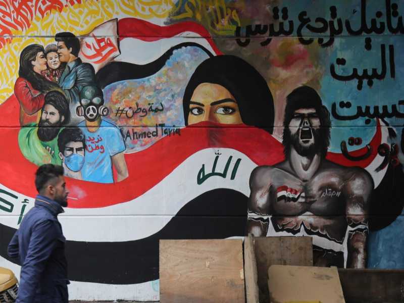 Un uomo cammina davanti a un murales che incita la rivolta a Piazza Tahrir, a Baghdad (foto LaPresse)