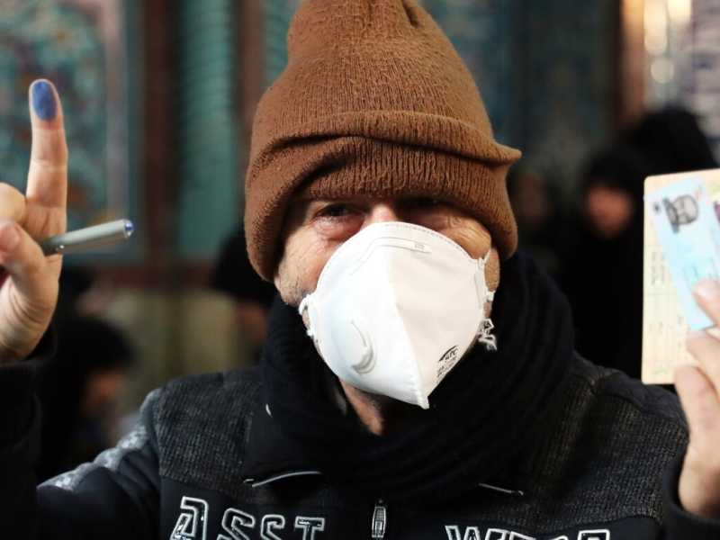 Un elettore, con la mascherina contro il virus, mostra il dito inchiostrato, dopo il voto alle elezioni parlamentari in un seggio di Teheran (foto Ebrahim Noroozi/LaPresse)