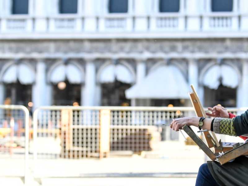 Una donna, con la mascherina, dipinge all'aria aperta in Piazza San Marco a Venezia (foto Claudio Furlan/LaPresse)