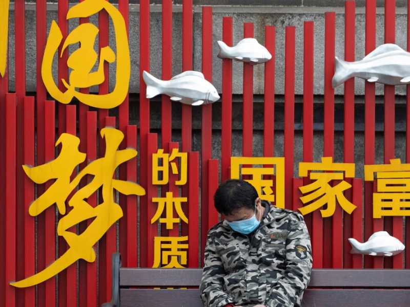 Wuhan, nei giorni scorsi: un uomo addormentato su una panchina. Sul muro lo slogan di propaganda governativa &ldquo;il sogno cinese&rdquo; (foto LaPresse)