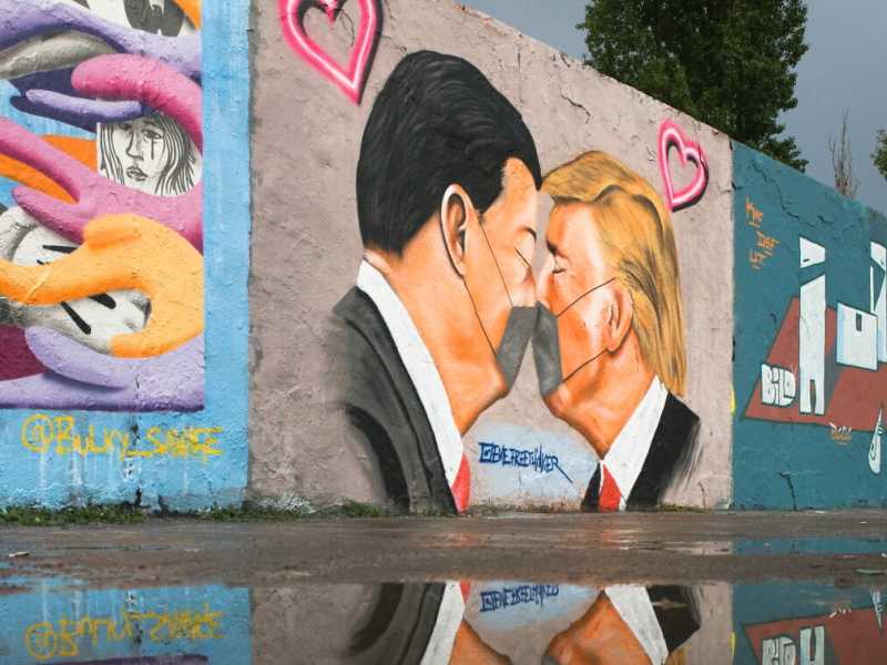 Una bambina corre di fronte al graffito che ritrae un bacio tra il presidente americano Trump e il presidente cinese Xi Jinping, nel parco pubblico Mauerpark di Berlino (Foto AP / Markus Schreiber)