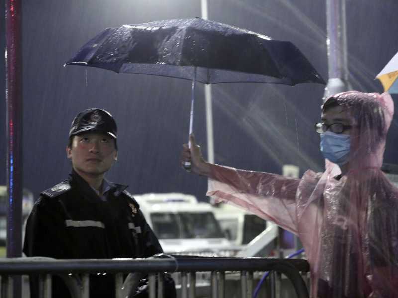 Un manifestante ripara un poliziotto dalla pioggia con un ombrello, ormai simbolo delle proteste di Hong Kong (foto AP)