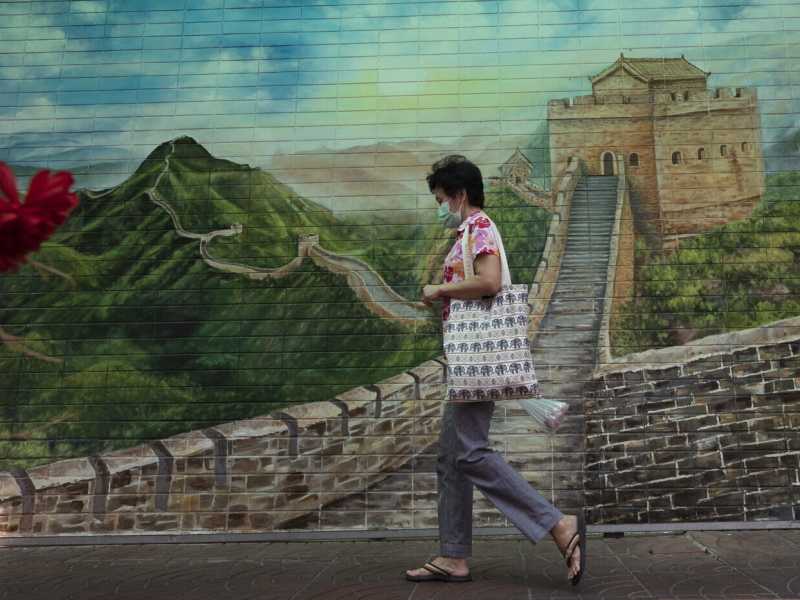 Una donna con mascherina protettiva di fronte a un dipinto della Grande muraglia cinese a Bangkok, in Thailandia (foto Ap/Sakchai Lalit)&nbsp;<br />