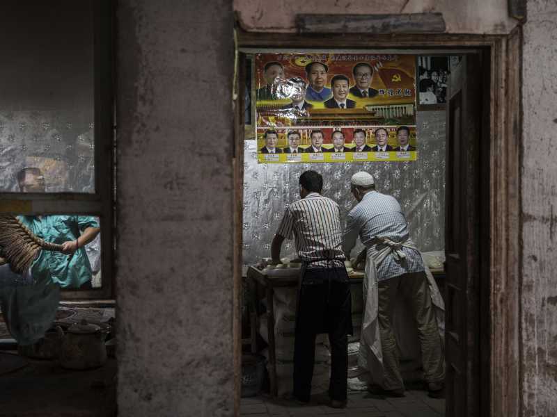 Sotto un poster con i leader cinesi, uomini uiguri impastano il pane, luglio 2017 nella città vecchia di Kashgar (foto di Kevin Frayer / Getty Images) <br />