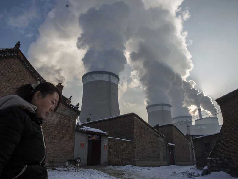 Una donna cinese esce dalla sua casa accanto a una centrale elettrica a carbone il 26 novembre 2015 nello Shanxi, in Cina (foto di Kevin Frayer / Getty Images)&nbsp;<br />