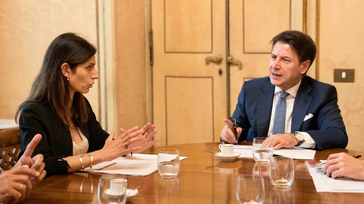 Immagine di Raggi e Conte sorridono insieme davanti ai fotografi, divisi però dal caso Primavalle