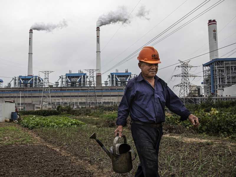 Un uomo annaffiare l'orto di fronte a una centrale elettrica a carbone il 13 ottobre 2021 a Hanchuan, provincia di Hubei, Cina (Getty Images)&nbsp;<br />