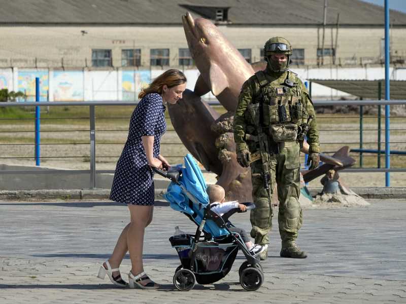 Una donna passeggia con il figlio nel passeggino di fronte a un soldato russo, a Kherson. (LaPresse)