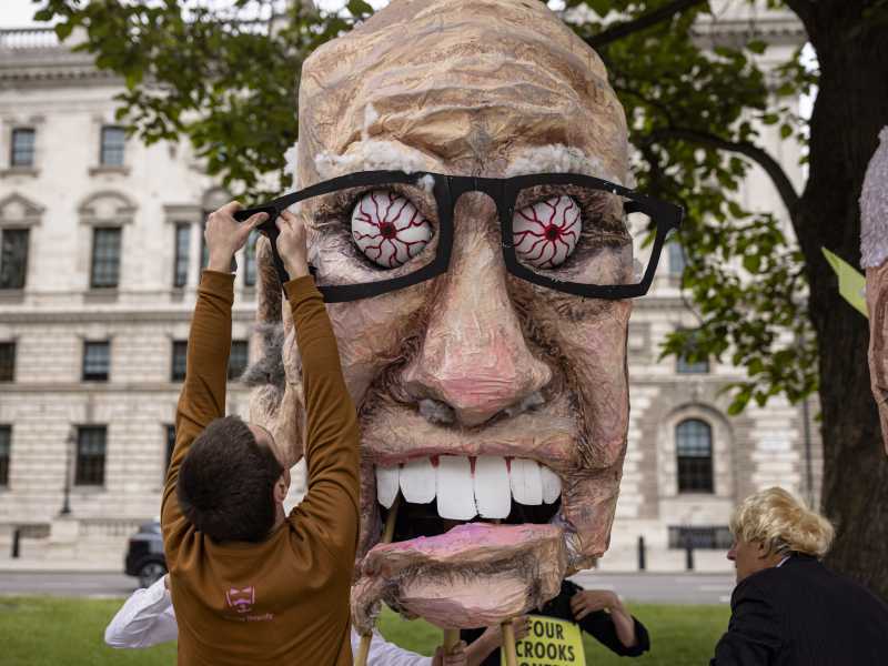 Un uomo usa del nastro adesivo per fissare gli occhiali a una testa di cartapesta di Rupert Murdoch a Londra (Rob Pinney/Getty Images)&nbsp;<br />