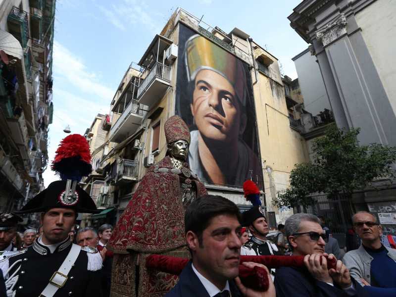 La processione del santo con sullo sfondo il murale di Jorit che lo raffigura (LaPresse)&nbsp;<br />