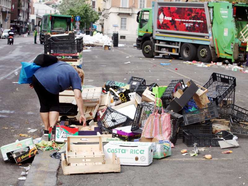 Una donna raccoglie la frutta buttata dopo il mercato di Papignano (MI) - foto LaPresse <br />