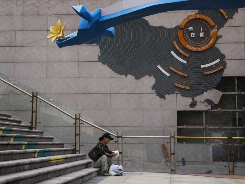 Una donna sistema la spesa vicino a una mappa che mostra i progetti di sviluppo di Evergrande, Pechino, 18 settembre 2023 (AP Photo/Andy Wong)&nbsp;<br />