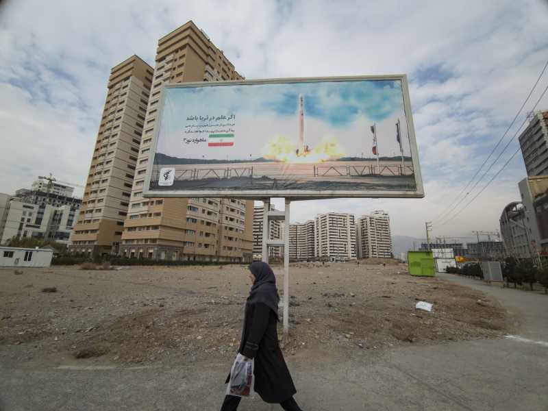 Una donna cammina sotto un cartellone della compagnia satellitare iraniana Qased in una zona residenziale di Teheran (Morteza Nikoubazl/NurPhoto) <br />