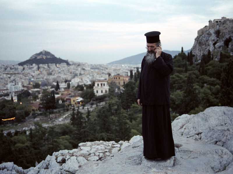 Un sacerdote parla al cellulare in cima alla collina dell'Are&ograve;pago ad Atene (Foto di Jean-Noel DE SOYE/via Getty Images)&nbsp;<br />