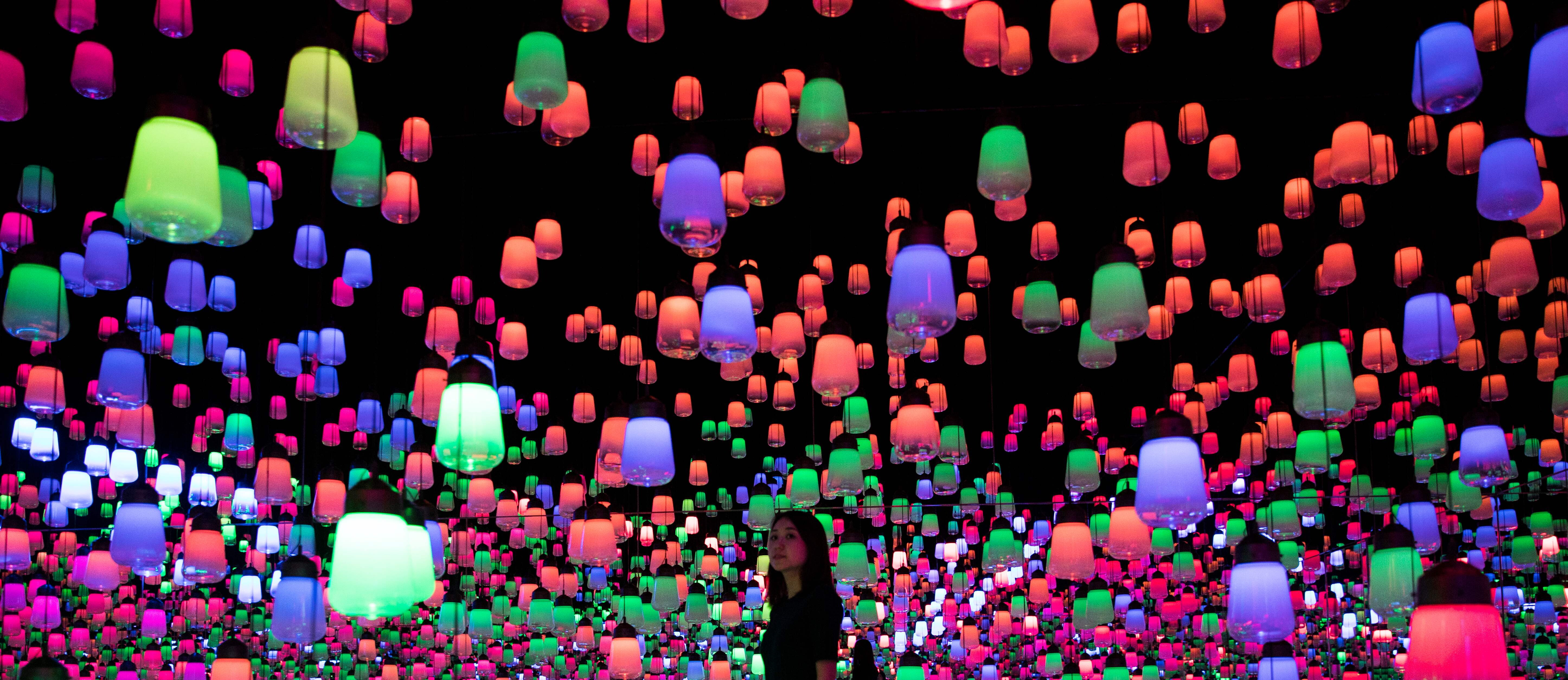 In questa foto scattata nel Mori building digital art museum di Tokyo il 1 maggio 2018 un membro del collettivo giapponese Teamlab cammina in mezzo all'installazione digitale fatta con lampade a sospensione, che si illuminano mentre il visitatore si avvicina e la luce si sposta da una lampada all'altra.
