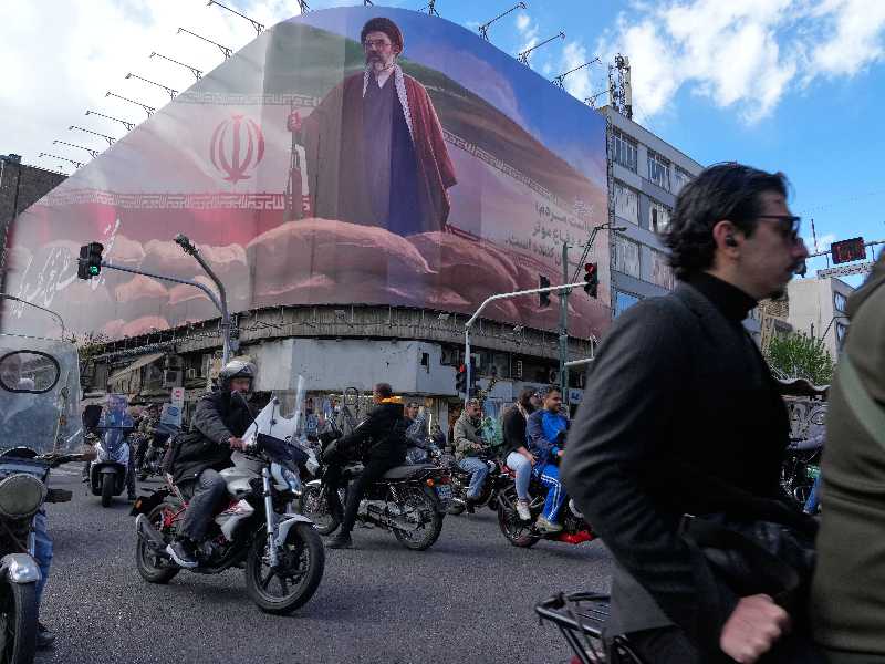 People drive their motorbikes past a billboard that shows a graphic depicting Iran's Supreme Leader Ayatollah Mojtaba Khamenei in downtown Tehran, Iran, Monday, April 6, 2026. (AP Photo/Vahid Salemi)