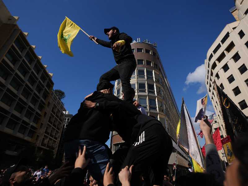 A protester stands on others' shoulders and waves a Hezbollah flag as demonstrators gather during a protest against Lebanese Prime Minister Nawaf Salam outside the government palace in Beirut, Lebanon, Saturday, April 11, 2026. (AP Photo/Hassan Ammar)